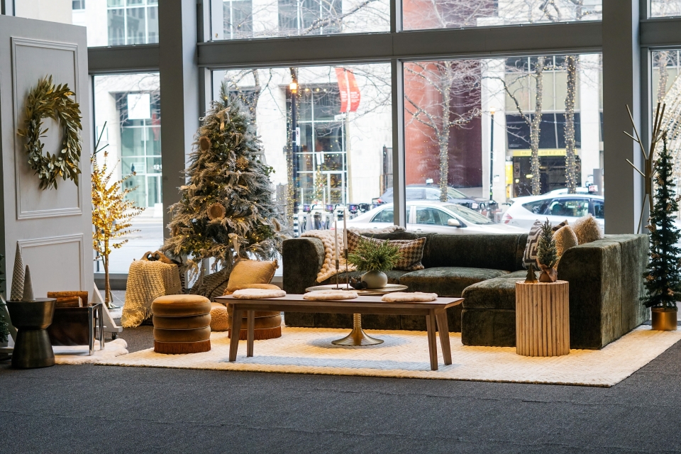 Salon constitué d'un fauteuil vert avec des coussins doux, une couronne de sapin, des petits bancs, une table basse, un sapin et des décorations festives hivernales.