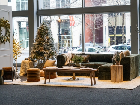 Salon constitué d'un fauteuil vert avec des coussins doux, une couronne de sapin, des petits bancs, une table basse, un sapin et des décorations festives hivernales.